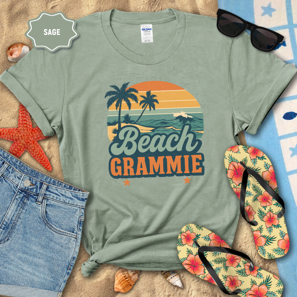 Sage green t-shirt with 'Beach Grammie' design on a sandy surface with beach-themed accessories.