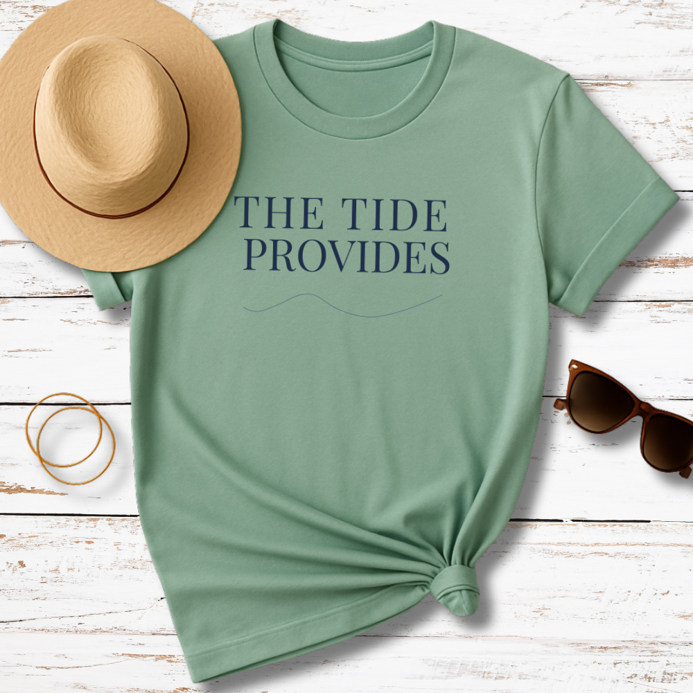 Green t-shirt with 'THE TIDE PROVIDES' text, accompanied by a hat, sunglasses, and bracelet on a wooden surface.