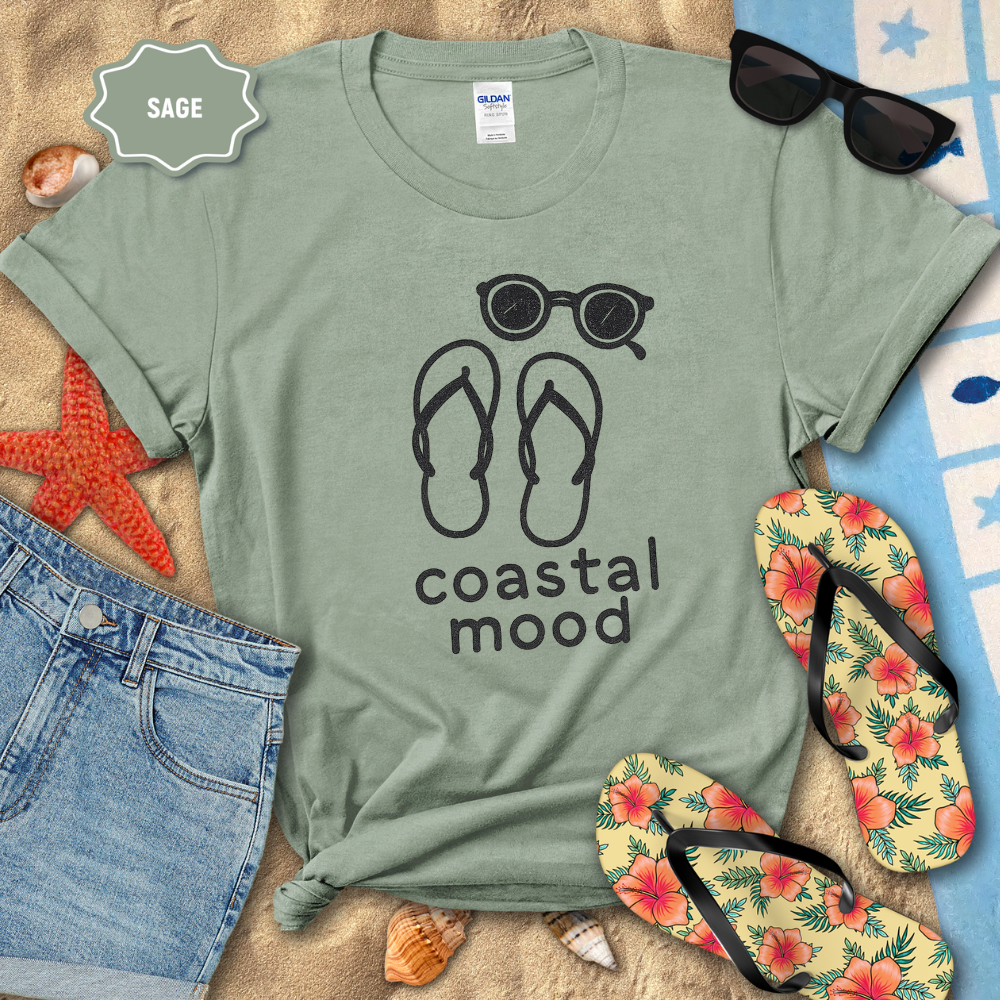 Sage green t-shirt with 'coastal mood' design on a beach-themed background