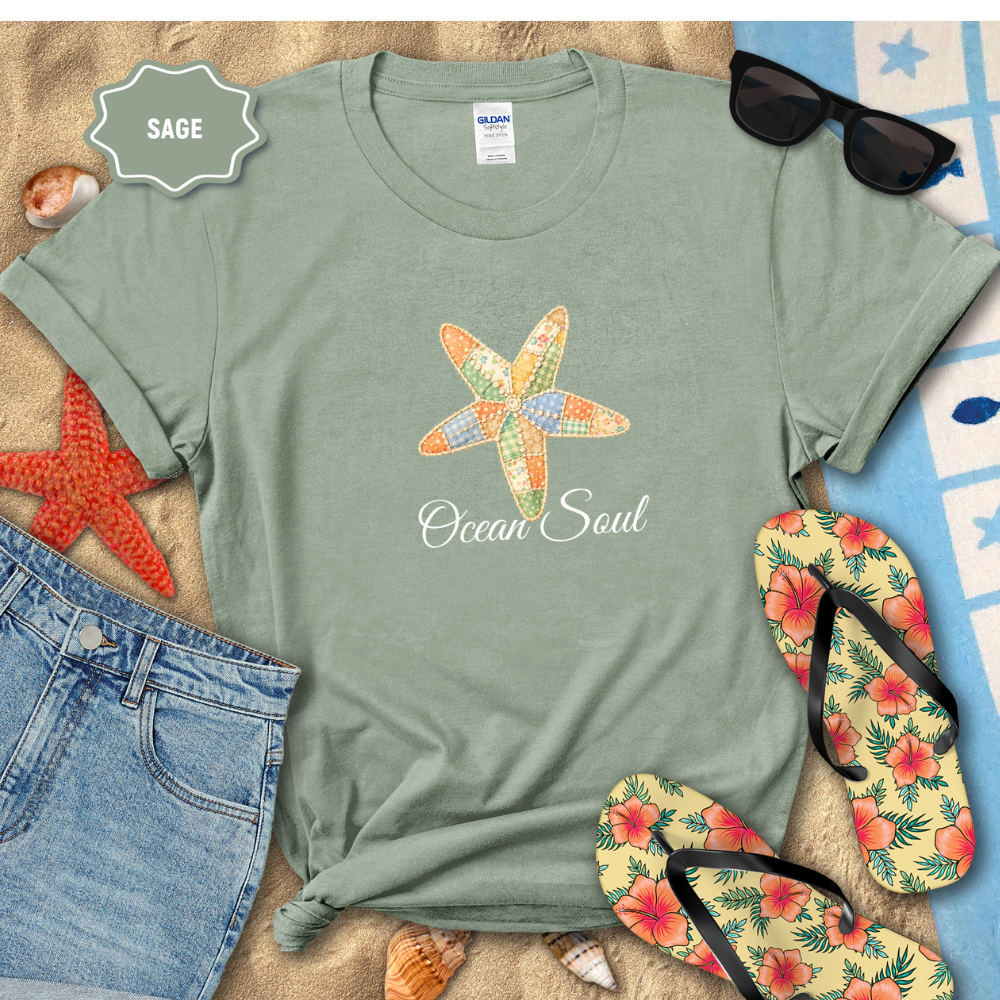 Sage green t-shirt with starfish design and 'Ocean Soul' text, surrounded by beach accessories on sand.