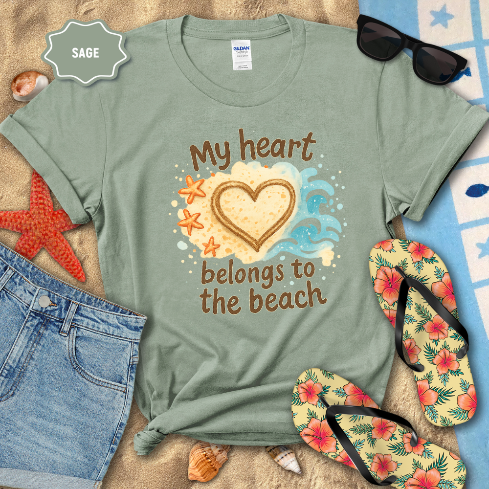 Sage green t-shirt with 'My heart belongs to the beach' design on a sandy background with sunglasses, flip-flops, and starfish.