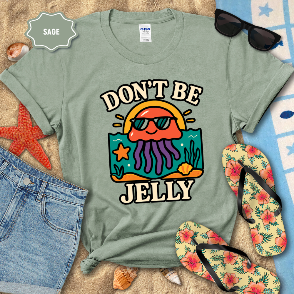 Sage green t-shirt with 'Don't Be Jelly' design on a beach setting with sunglasses, flip-flops, and starfish.