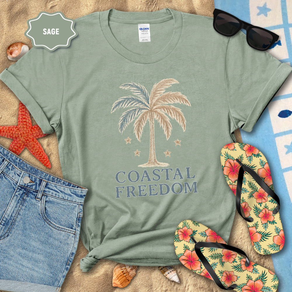 Sage green t-shirt with palm tree design and 'Coastal Freedom' text, surrounded by beach accessories.