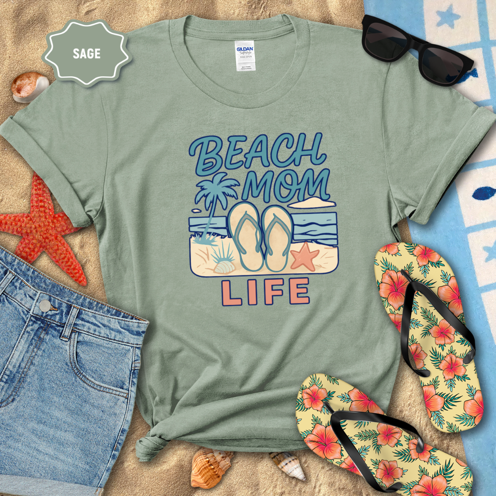 Sage green t-shirt with 'Beach Mom Life' design on a sandy background with flip-flops and sunglasses.