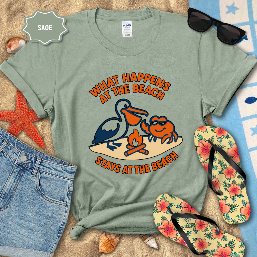 Sage green t-shirt with beach graphic and text, surrounded by beach accessories on sand.