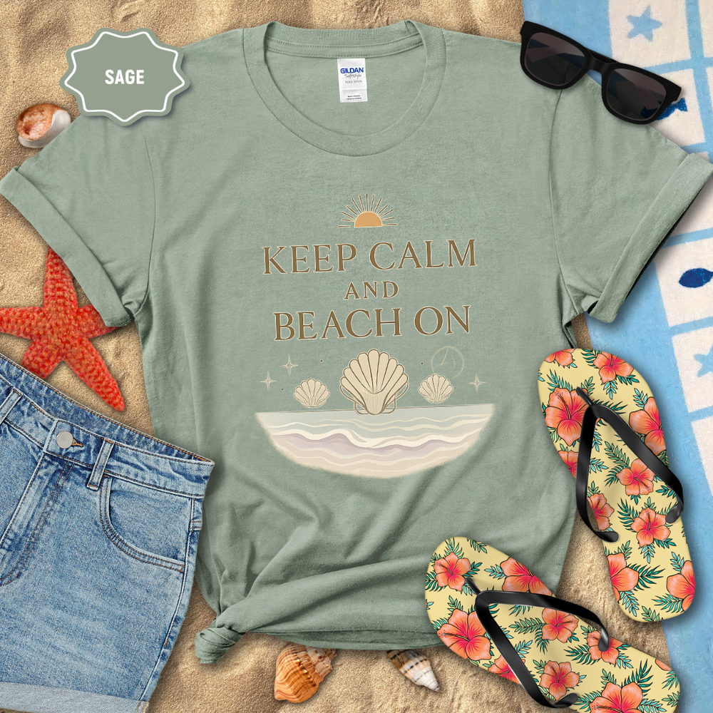 Sage green t-shirt with 'Keep Calm and Beach On' design on a sandy background with beach accessories.