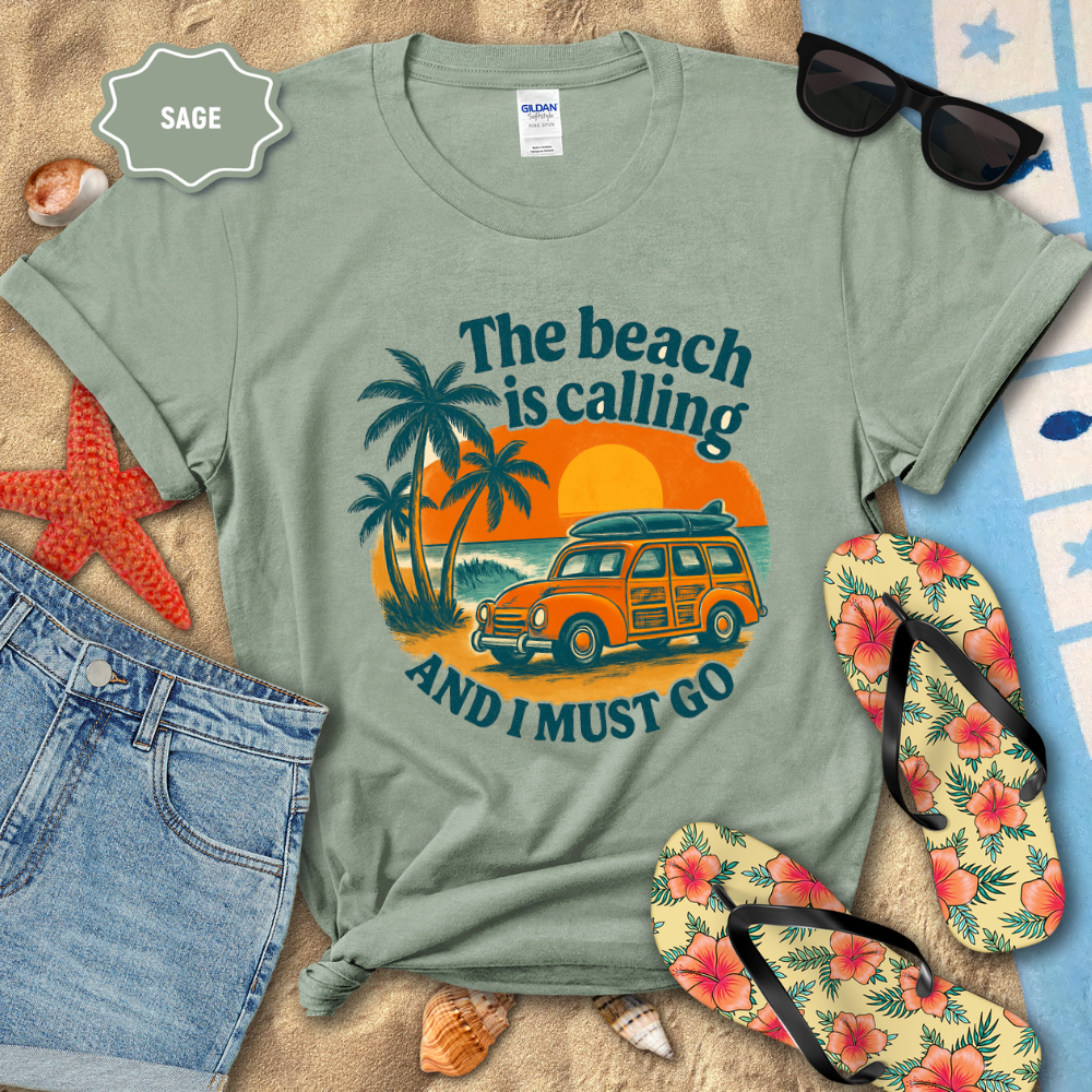 Sage green t-shirt with beach-themed design on a sandy background with flip-flops and sunglasses.