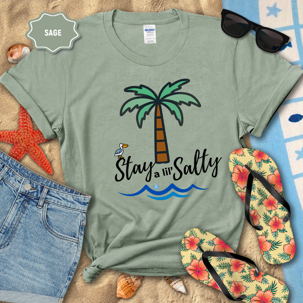 Sage green t-shirt with palm tree and 'Stay a lil' Salty' text on a beach-themed background.