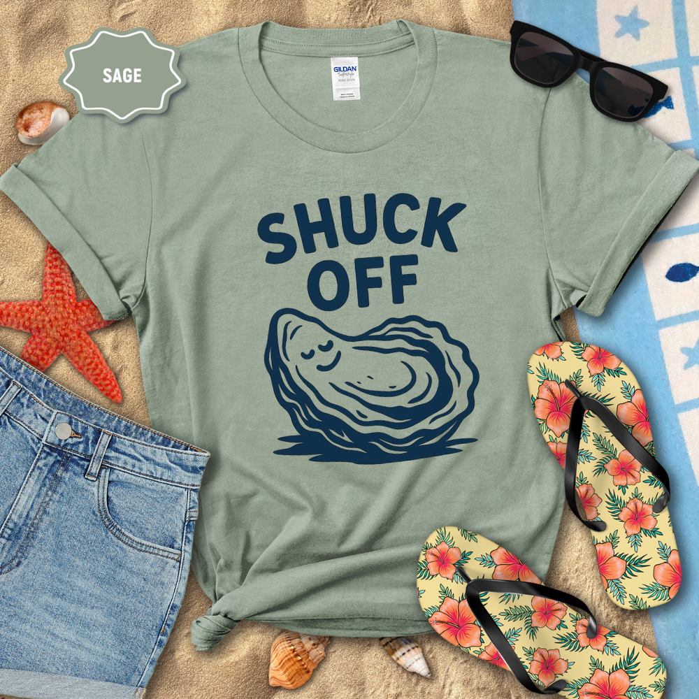 Sage green t-shirt with oyster graphic and 'SHUCK OFF' text on a beach setting with sunglasses, flip-flops, and starfish.