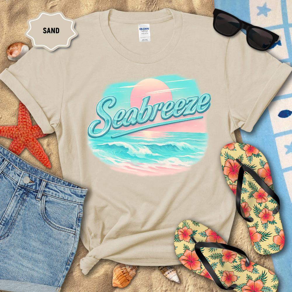 Beige t-shirt with 'Seabreeze' design on a sandy background with sunglasses, flip-flops, and beach accessories.