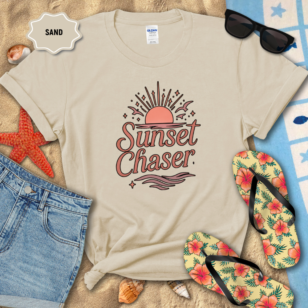Beige t-shirt with 'Sunset Chaser' design on a sandy background with beach accessories.