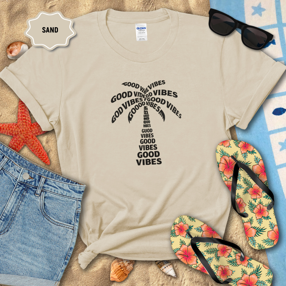 Beige t-shirt with 'Good Vibes' text, sunglasses, flip-flops, and beach items on sand