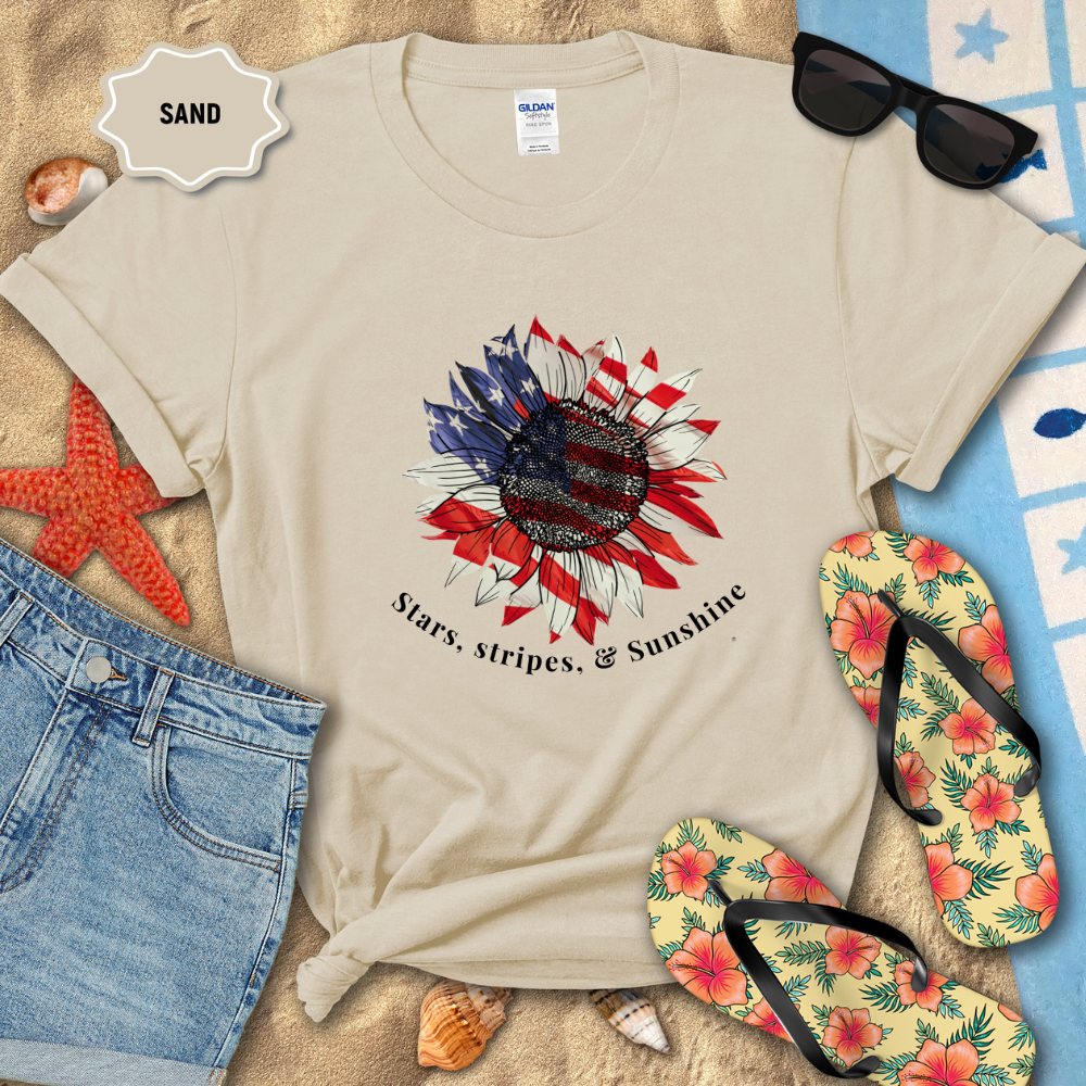 Beige t-shirt with a sunflower design and text on a sandy background with flip-flops and sunglasses.