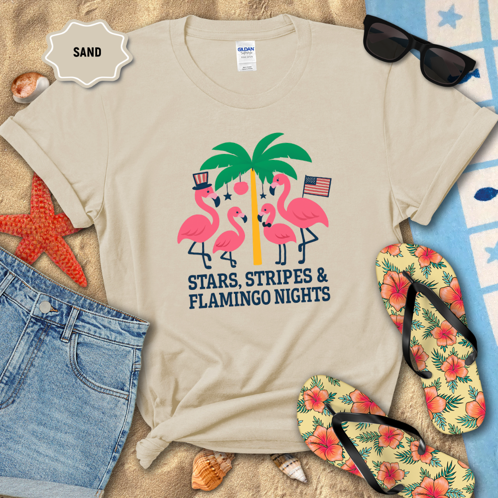 Beige t-shirt with flamingo design on sand with sunglasses, flip-flops, and beach accessories.