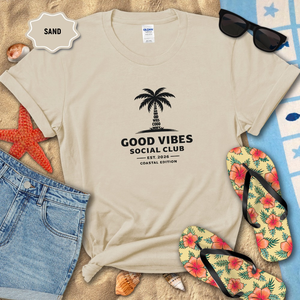 Beige t-shirt with 'Good Vibes Social Club' design on a sandy background with flip-flops and sunglasses.