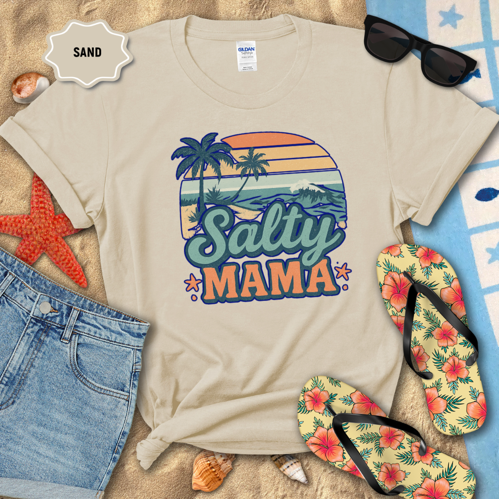 Beige t-shirt with 'Salty Mama' design on a sandy background with sunglasses, flip-flops, and beach accessories.