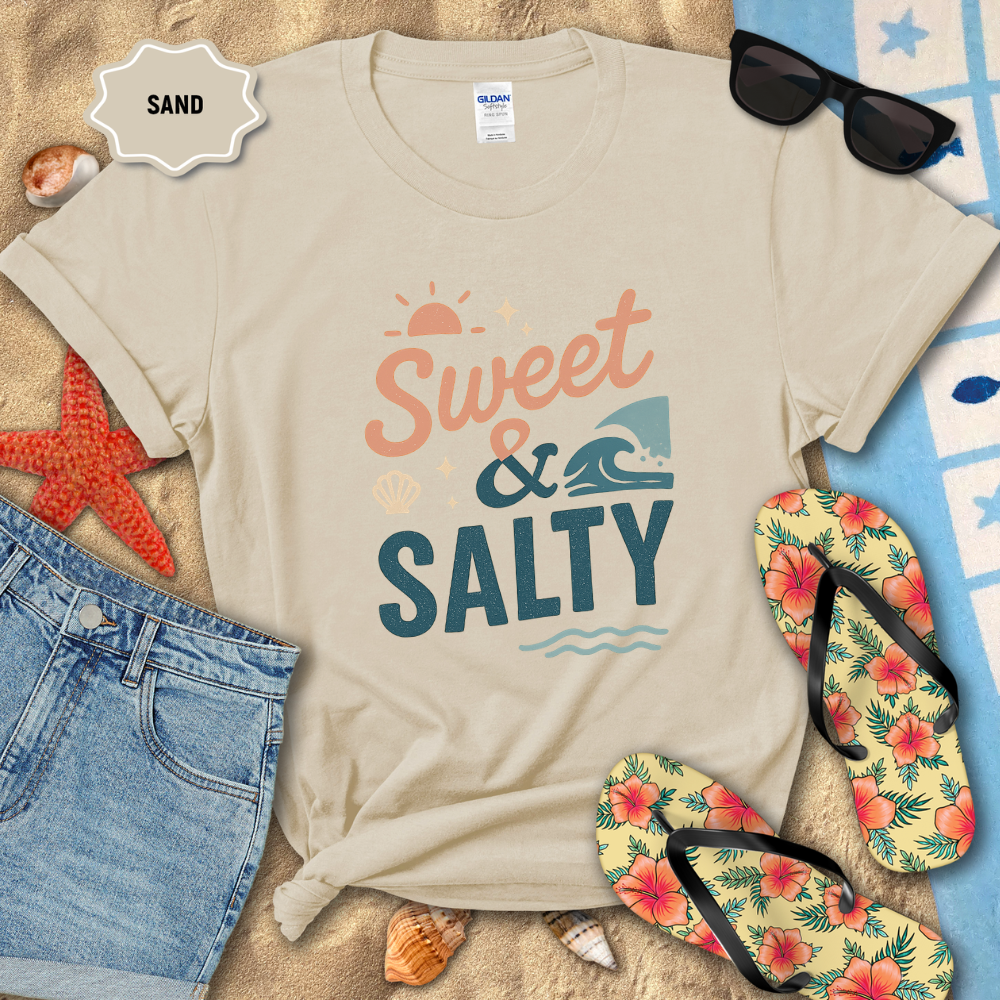 Beige t-shirt with 'Sweet & Salty' text on a sandy background with beach accessories.