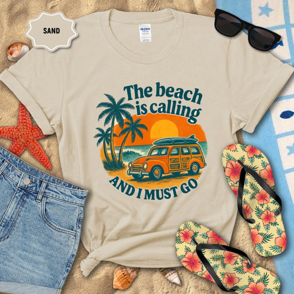 Beige t-shirt with beach-themed design on sand with sunglasses, flip-flops, and denim shorts.