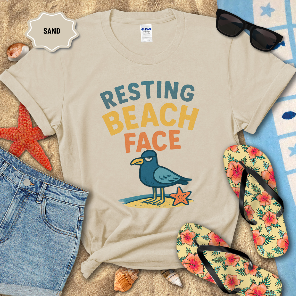 Beige t-shirt with 'Resting Beach Face' design on sand with beach accessories.