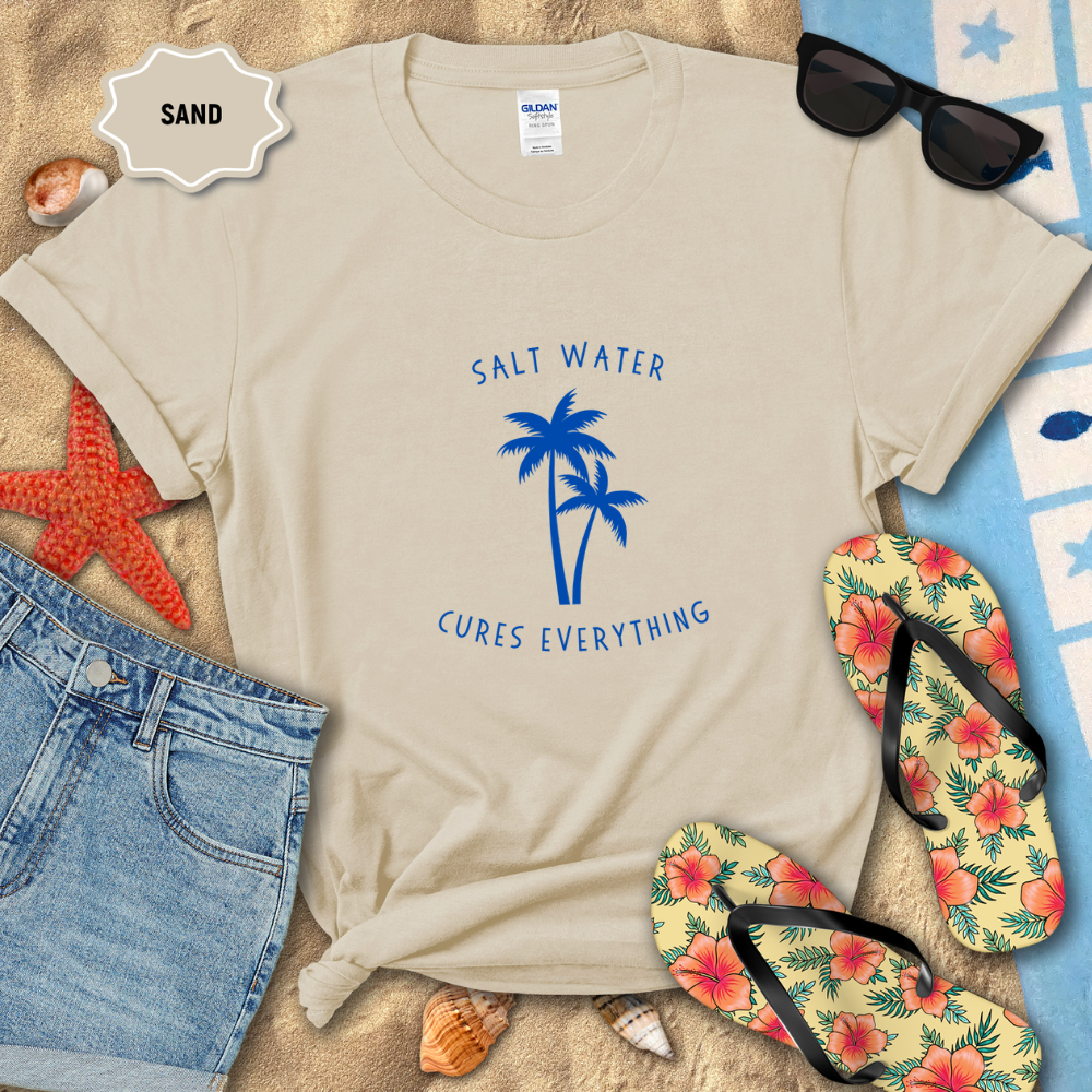Beige t-shirt with 'Salt Water Cures Everything' design on sand with beach accessories.
