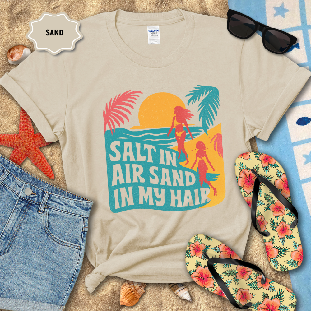 Beige t-shirt with beach-themed design and accessories on sand