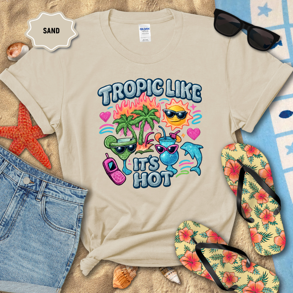 Beige t-shirt with tropical-themed design on a sandy background with beach accessories.