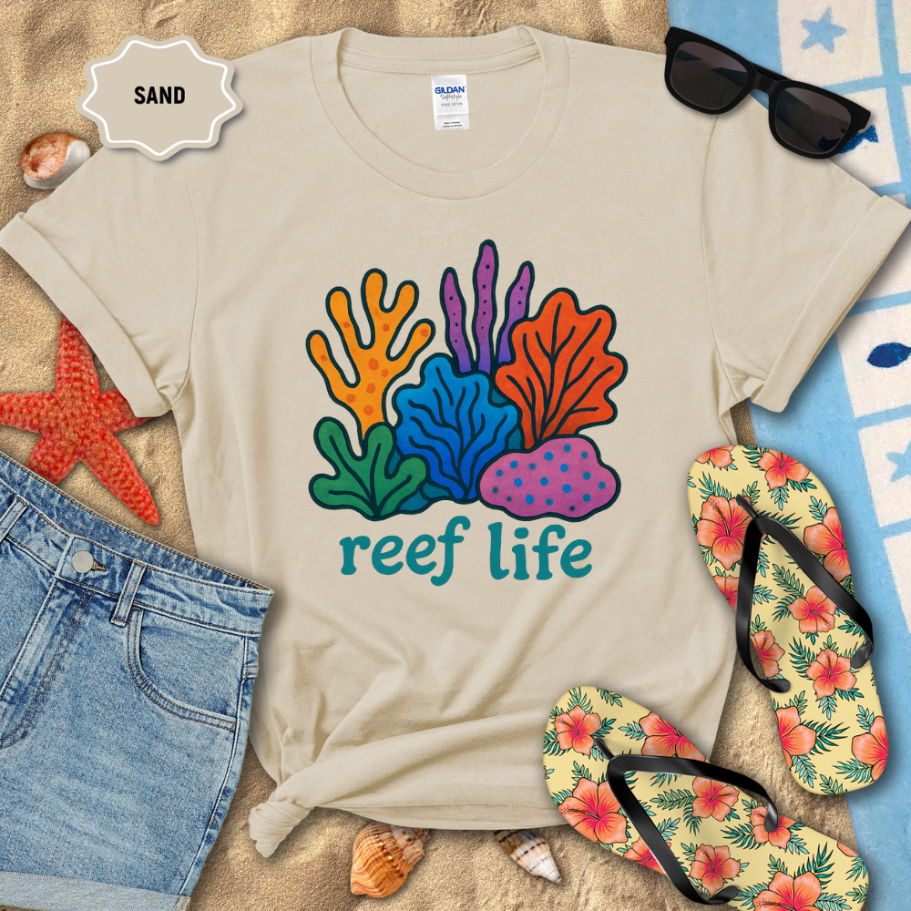 Beige t-shirt with 'reef life' design on sand with beach accessories.