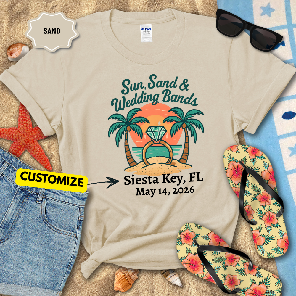 Beige t-shirt with 'Sun, Sand & Wedding Bands' design on sand with beach accessories.