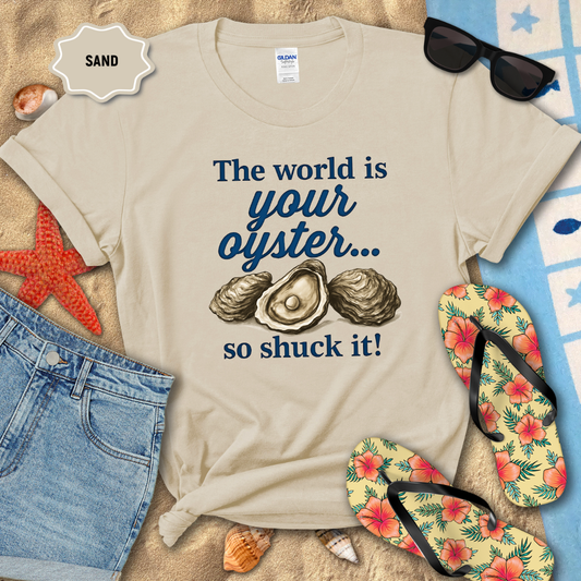 Beige t-shirt with oyster graphic and text on a sandy background with beach accessories.