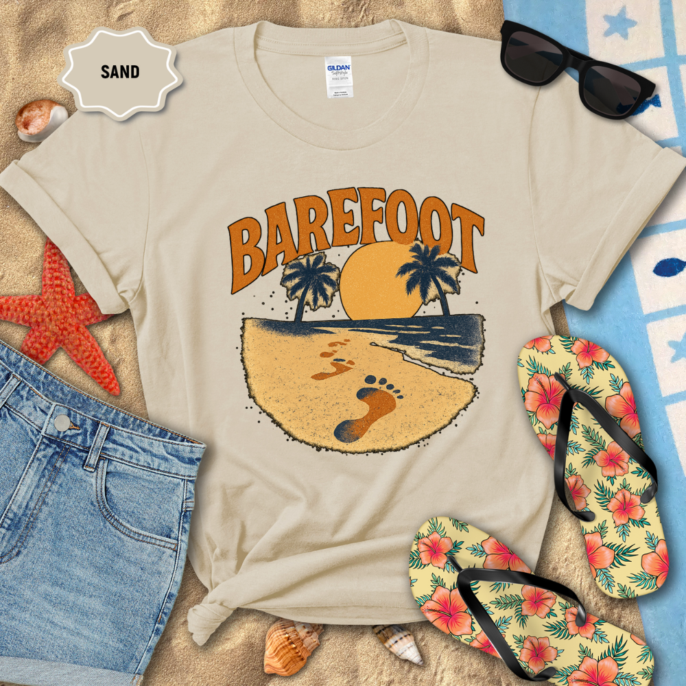 Beige t-shirt with 'Barefoot' design on sand with sunglasses, flip-flops, and beach accessories.