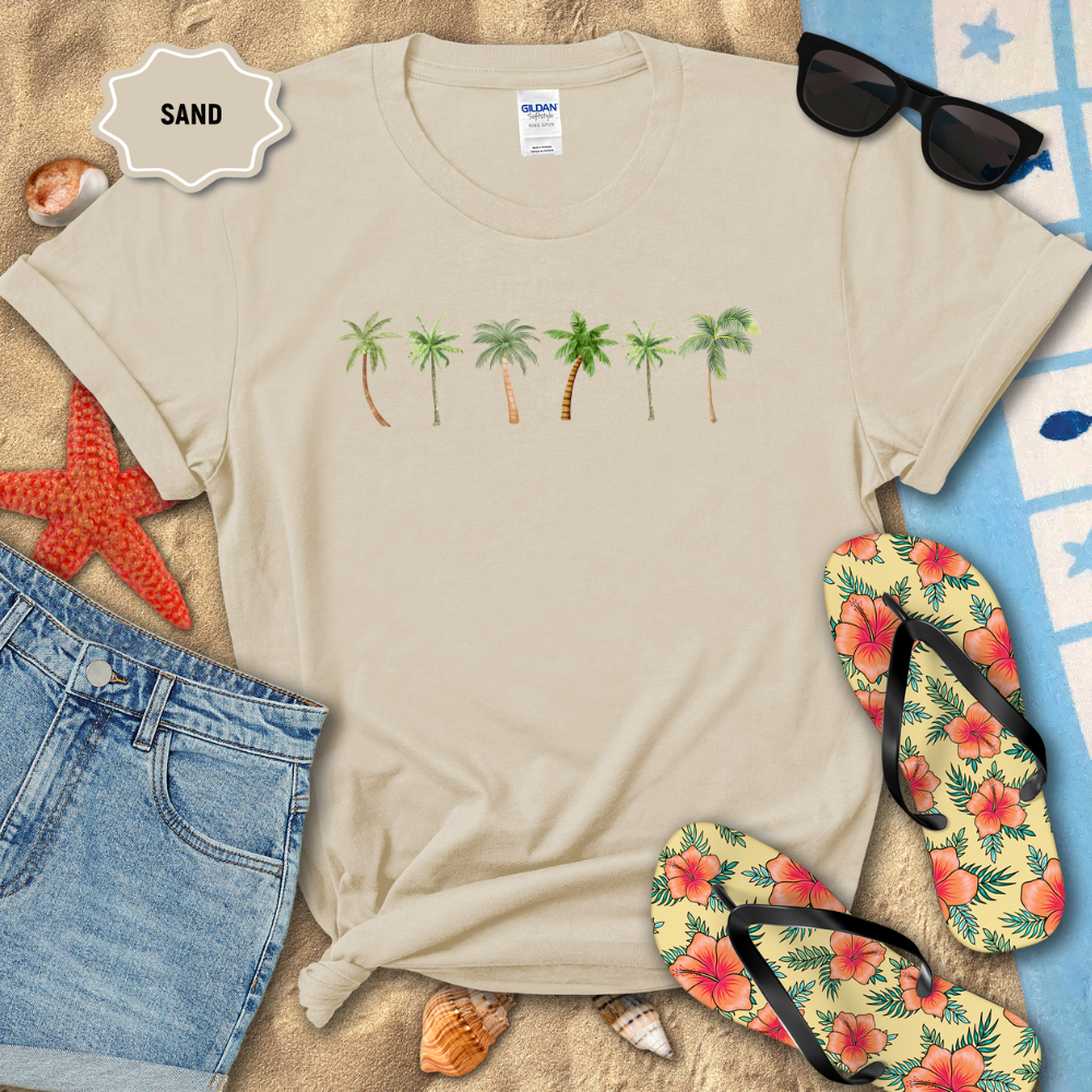 Beige t-shirt with palm tree design on a sandy background with flip-flops and sunglasses.