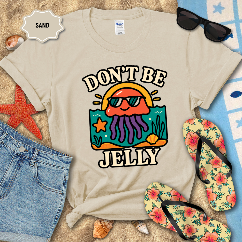 Beige t-shirt with 'Don't Be Jelly' design on a sandy background with beach accessories.