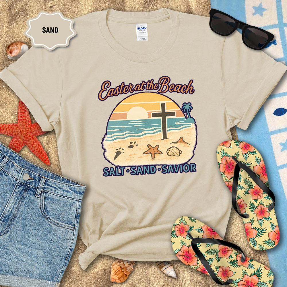 Beige t-shirt with beach-themed design on sand with sunglasses, flip-flops, and starfish.