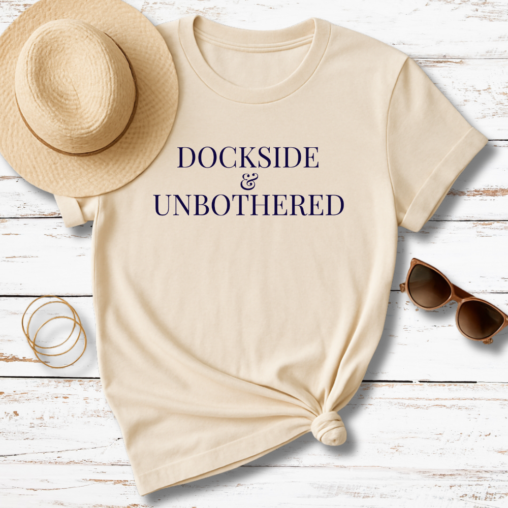 Beige t-shirt with 'THE TIDE PROVIDES' text, sun hat, sunglasses, and bracelet on a wooden surface