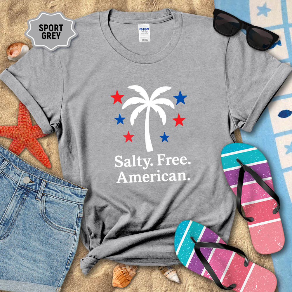 Gray t-shirt with palm tree and stars design on a sandy background with beach accessories.