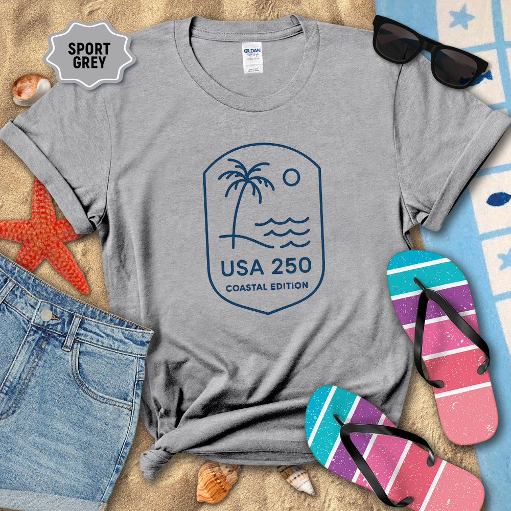 Gray t-shirt with a beach-themed design on sand with flip-flops and sunglasses.