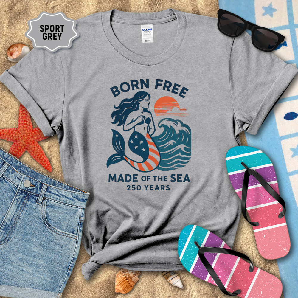 Gray t-shirt with mermaid design on a sandy background with beach accessories.