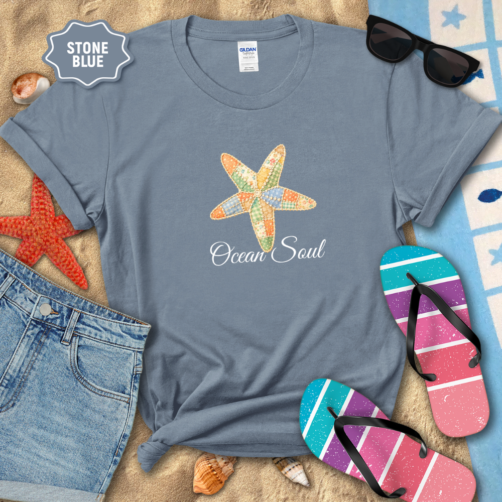 Stone blue t-shirt with starfish design and 'Ocean Soul' text, surrounded by beach accessories on sand.