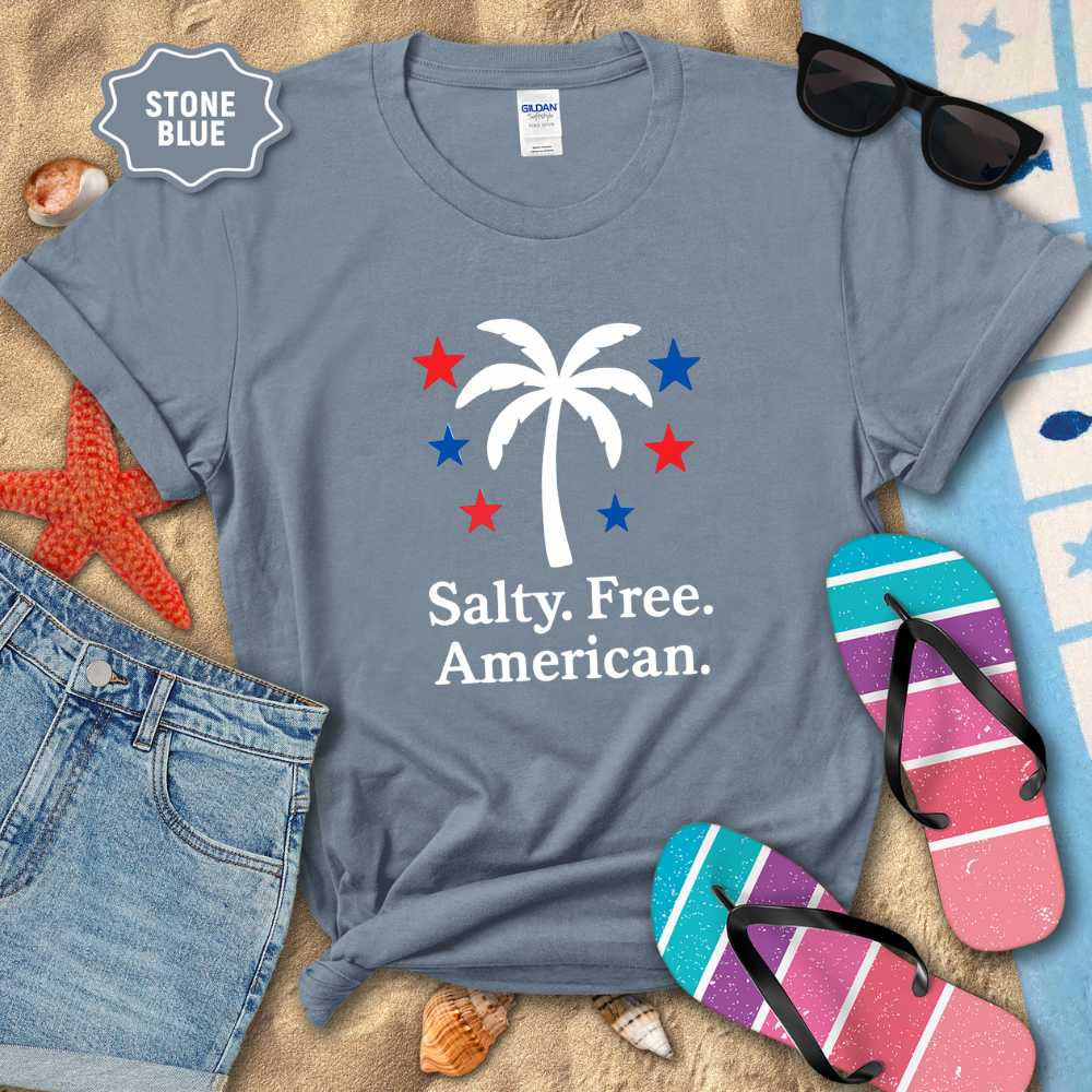 Stone blue t-shirt with palm tree and stars design on a sandy background with beach accessories.