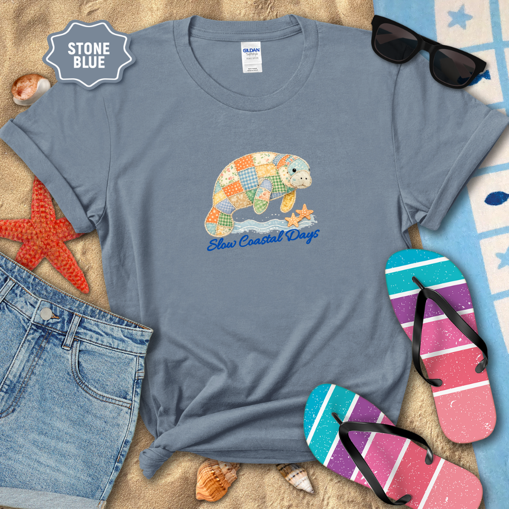 Stone blue t-shirt with a colorful sea turtle graphic and 'Blue Coastal Days' text, surrounded by beach items.