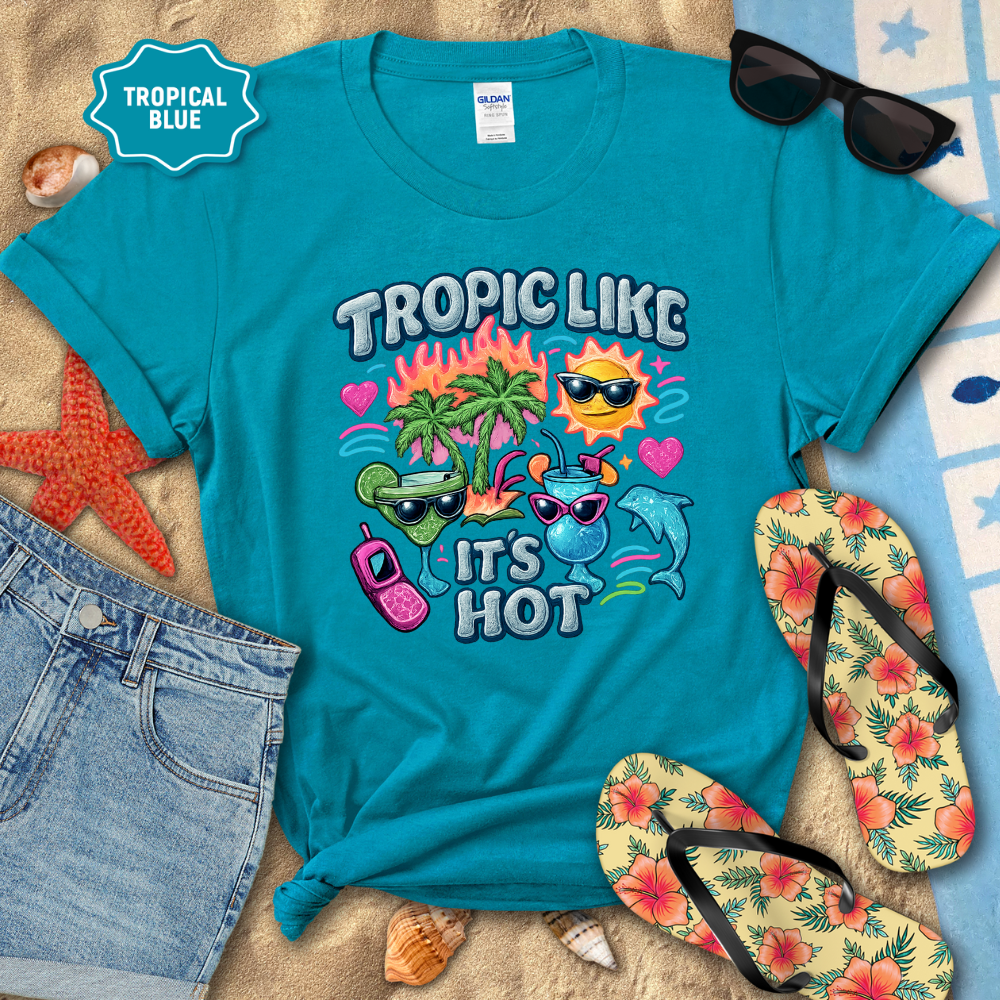 Turquoise t-shirt with tropical-themed design on a sandy background with beach accessories.