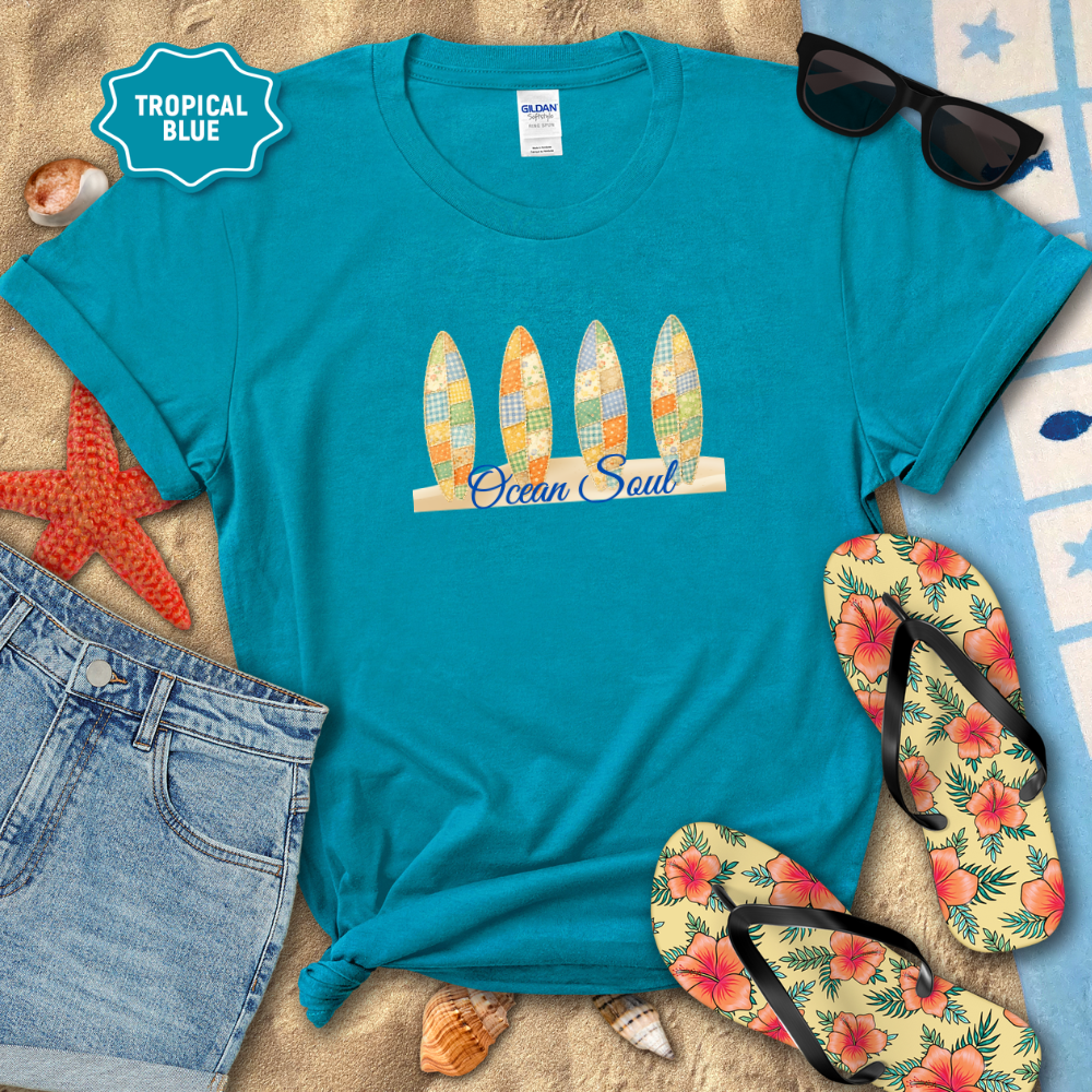 Blue t-shirt with 'Ocean Soul' design, sunglasses, flip-flops, and beach accessories on a sandy background.