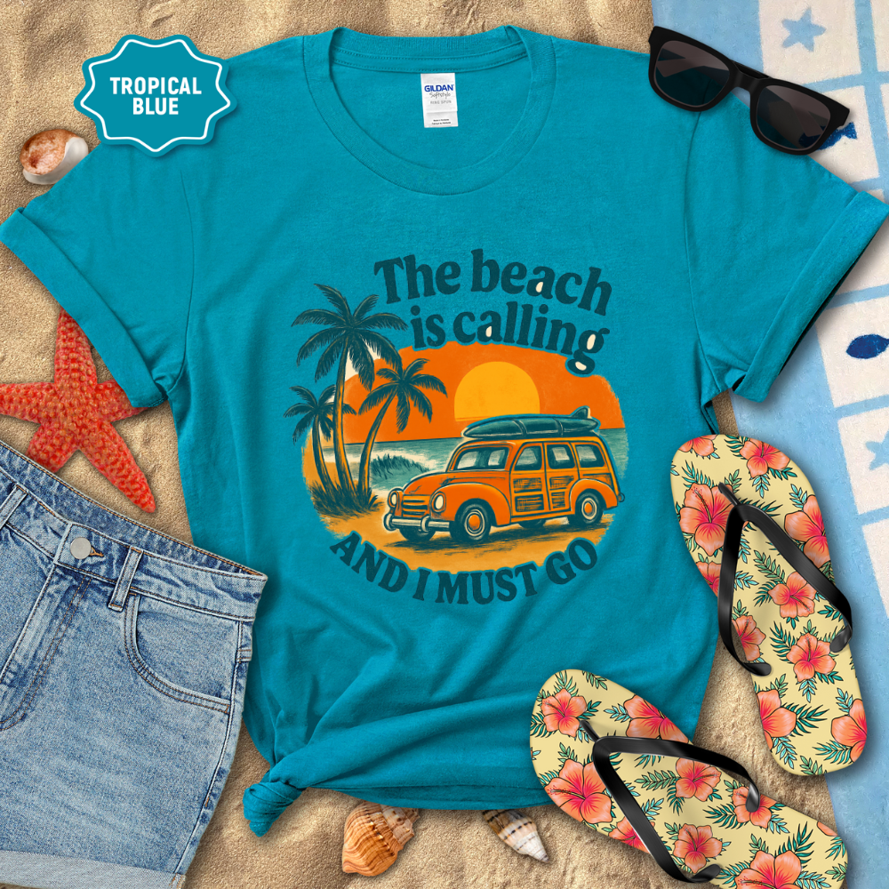 Blue t-shirt with beach-themed design on a sandy background with flip-flops and sunglasses.