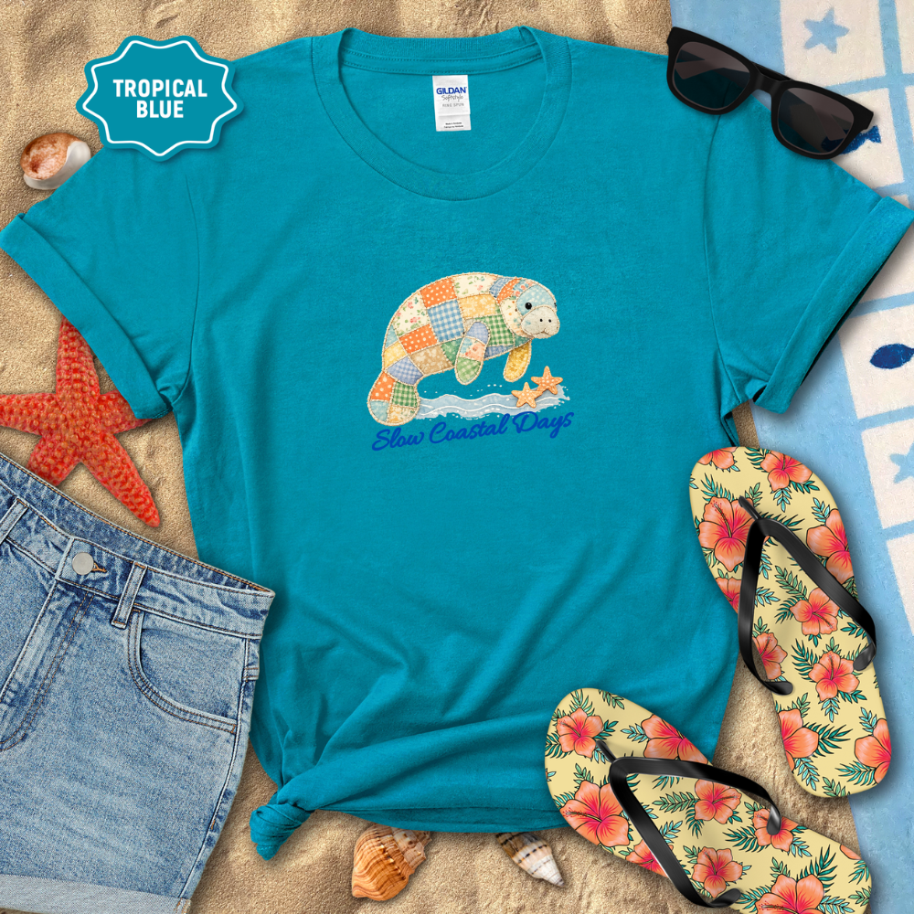Blue t-shirt with a turtle design on a sandy background with flip-flops and sunglasses.