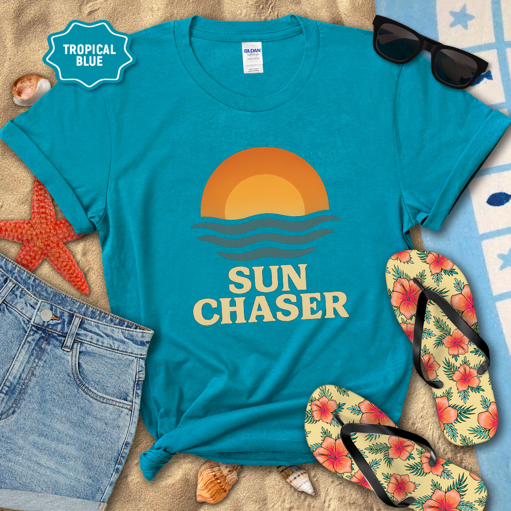 Blue t-shirt with 'Sun Chaser' design on a sandy background with flip-flops and sunglasses.