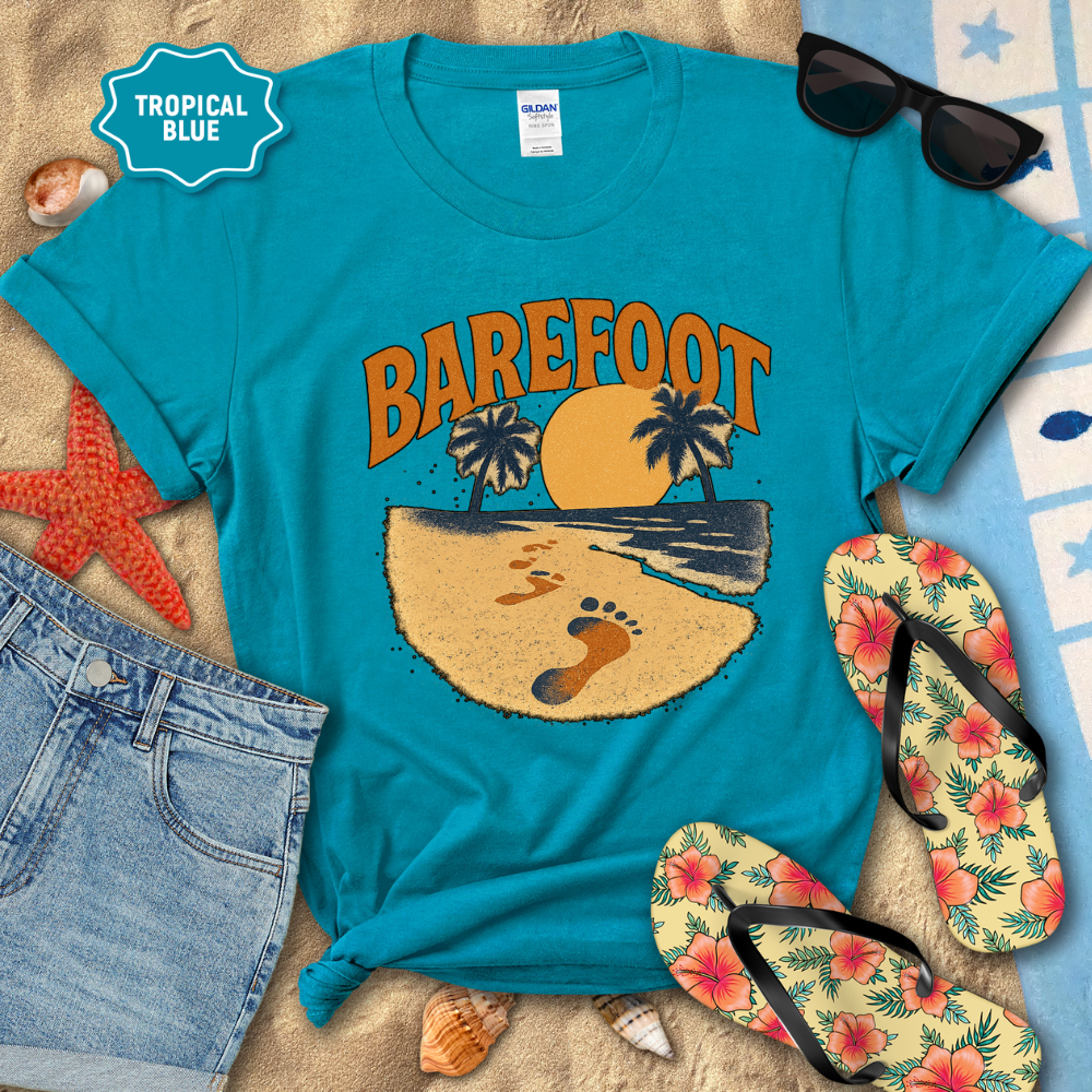 Blue t-shirt with 'Barefoot' graphic design on a sandy background with flip-flops and sunglasses.