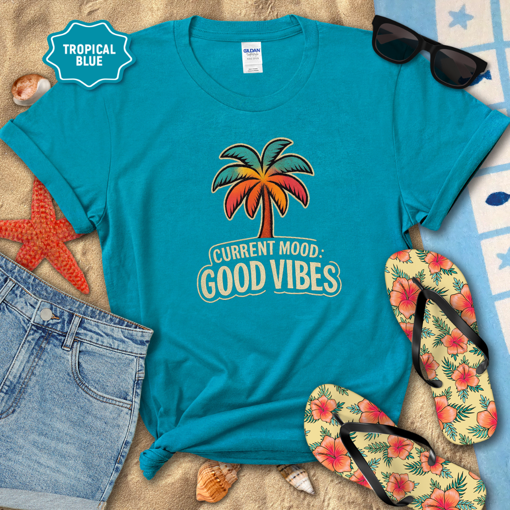 Turquoise t-shirt with palm tree design and 'Current Mood: Good Vibes' text, surrounded by beach accessories.