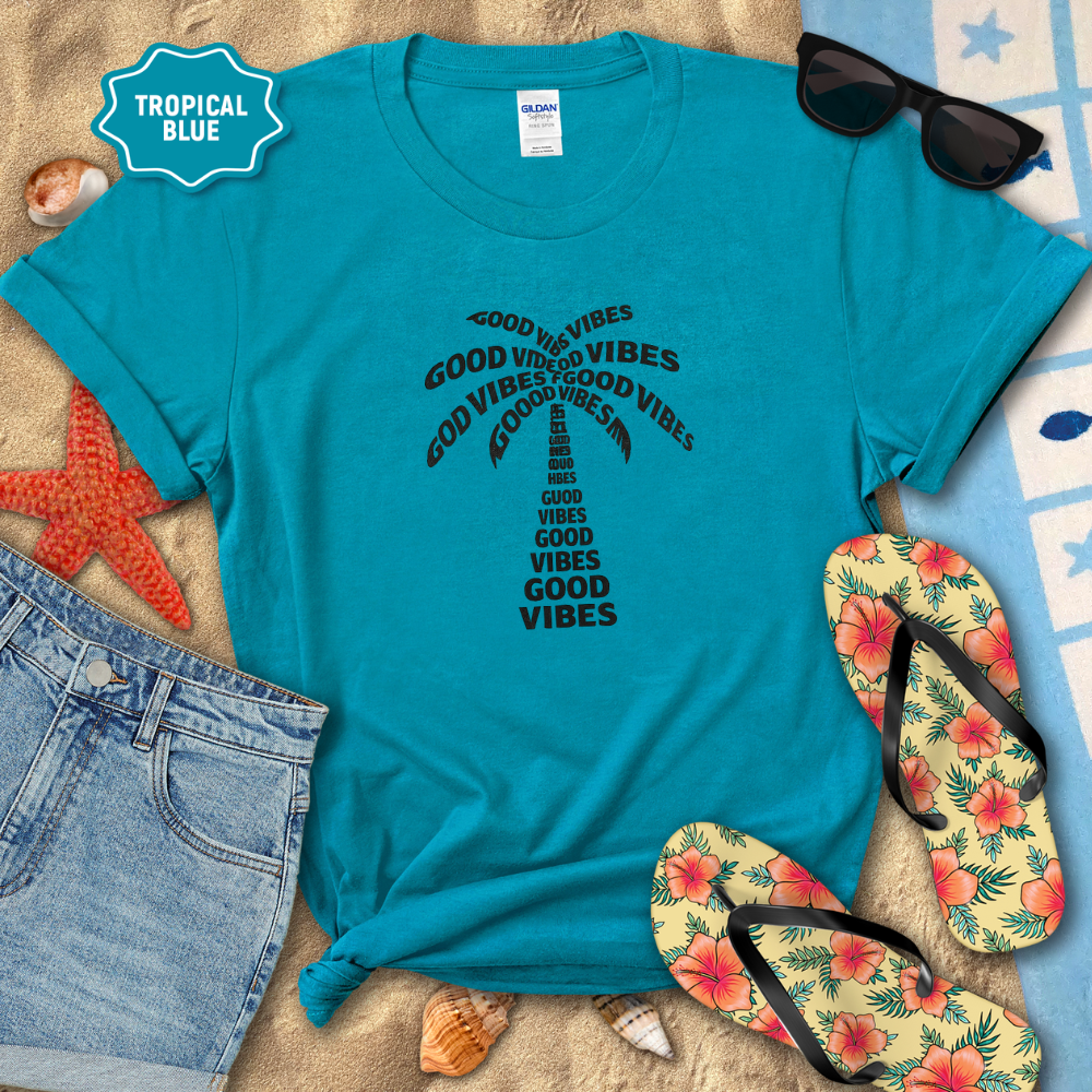 Turquoise t-shirt with 'Good Vibes' text, sunglasses, flip-flops, and beach accessories on a sandy background.