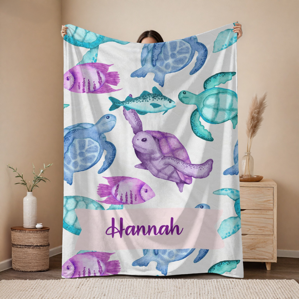 Person holding a colorful towel with sea turtle and fish patterns and the name 'Hannah' on a beige background.