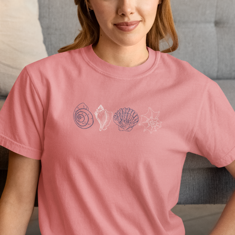 Smiling woman wearing a peony Comfort Colors t-shirt with minimalist coastal shell design.